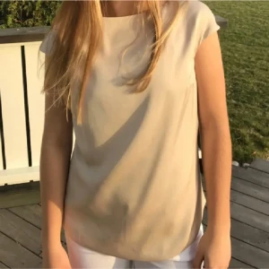 Blus - Supersnygg beige blus från Ahlvar Gallery i lyxigt sidenmaterial. Modellen är ärmlös med rund halsringning och har en clean, minimalistisk look. Perfekt att styla med jeans eller kjol för en fräsch vibe.