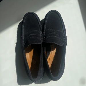 Blåa mockaloafers från Polo Ralph Lauren - Stilrena blåa loafers i mocka från Polo Ralph Lauren. Skorna har klassisk penny loafer-design med rund tå och platt sula med gummidetaljer undertill för extra grepp.