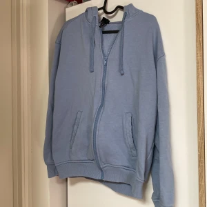 Ljusblå hoodie från H&M, relaxed fit - Ljusblå hoodie från H&M i relaxed fit med dragkedja framtill, huva med snörning och två fickor. Tillverkad i mjuk bomullsblandning, perfekt för chill dagar. Långärmad och ribbade muddar vid ärmslut och nederkant. Tecken på användning men säljer för väldigt lågt pris, övriga frågor så är det bara kontakta mig  eller köp direkt!  