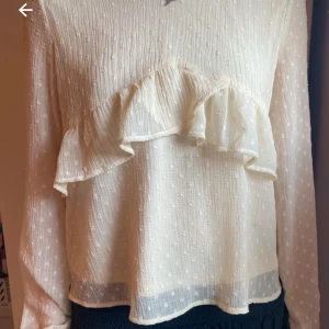 Kräm vit blus - En gullig blus med en liten v ringning och en volang runt hela kroppen. Passar perfekt med ett par Jens och vit tillfällen där du vill vara lite finare.
