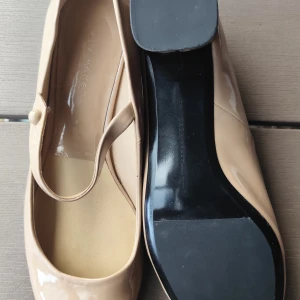 Beige ballerinaskor från Zara Woman - Snygga beige ballerinaskor i lack från Zara Woman med rund tå och en klassisk rem över foten. Skorna har platt sula och en stilren look som passar till många outfits. Perfekta för dig som gillar enkel och elegant stil.