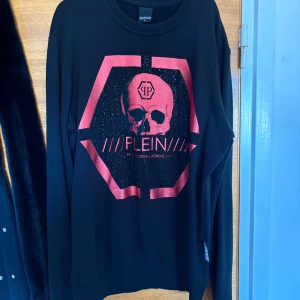 Svart tröja med dödskalle från Philipp Plein - Cool svart tröja från Philipp Plein med ett stort rött tryck framtill som visar en dödskalle och logga.                                                                                       Pris kan diskuteras 