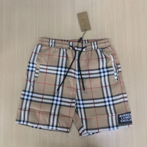 Beige rutiga shorts Burberry - Snygga beige shorts från Burberry med klassiskt rutigt mönster i svart, vitt och rött. Shortsen har elastisk midja med svart snörning och sidofickor. Perfekta för sommaren 