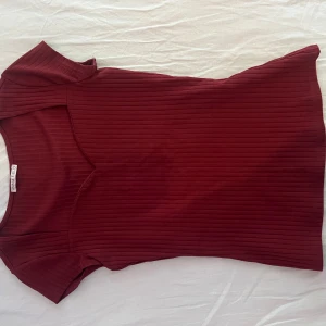 Ribbad vinröd topp från Anna Field - Vinröd ribbad topp från Anna Field med korta ärmar och rund halsringning. Toppens material är stretchigt och följsamt, perfekt för en stilren och enkel look. Den har en slim passform och är lätt att matcha med både jeans och kjol. Storlek S/M. Aldrig använt. 