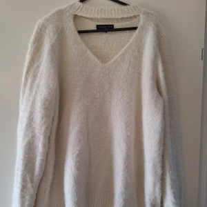 Vit fluffig stickad tröja F&F - Supermjuk och fluffig vit stickad tröja från F&F med v-ringning och lång ärm. Oversized känsla och ribbad kant vid halsen. Perfekt för lager-på-lager och chill dagar. Materialet är en mix av polyamid och akryl för extra mysfaktor.