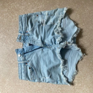 Ljusblå jeansshorts från Divided - Säljer ett par ljusblå jeansshorts från Divided i storlek 36. Shortsen har hög midja, slitna detaljer och fransiga kanter för en avslappnad vibe. Klassisk femficksmodell med knapp och dragkedja framtill. Perfekta för sommaren!