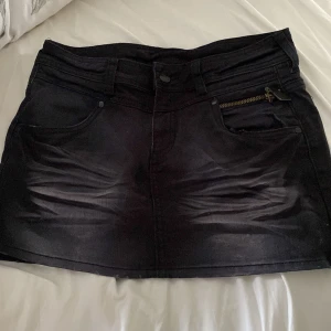 Svart jeanskjol från H&M - Svart kort jeanskjol från H&M med klassiska fickor fram och bak, dragkedjedetalj på ena fickan och bälteshällor. Gjord i stretchig bomullsblandning för en bekväm passform. Perfekt till sneakers eller boots.