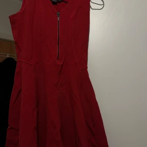 Röd kort klänning från Armani Exchange - Snygg röd ärmlös klänning från Armani Exchange med markerad midja och dragkedja framtill. Modellen är kort och har en lätt utställd kjol, perfekt för dig som gillar en stilren och modern look. Materialet känns mjukt och följsamt.