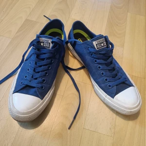 Blå Converse All Star sneakers - Snygga blå Converse All Star sneakers med klassisk vit tå och sula. Skorna har snörning och är tillverkade i canvas med innersula i Lunarlon för extra komfort. Perfekta för dig som gillar en tidlös och avslappnad stil.