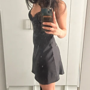 Svart spetsklänning med smala axelband - Supersnygg svart kort klänning med smala axelband och spetsdetaljer upptill. Djup v-ringning och genombruten spets över byst och midja ger en riktigt chic vibe. Kjolen är slät och lätt utsvängd. Perfekt för dig som vill sticka ut.