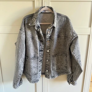 Grå oversized jeansjacka från ZARA - Säljer en grå, oversized jeansjacka från ZARA med cool tvättad look. Jackan har stora fickor framtill, klassisk krage och knappar längs hela framsidan. Perfekt att slänga över en hoodie eller t-shirt för en chill vibe.