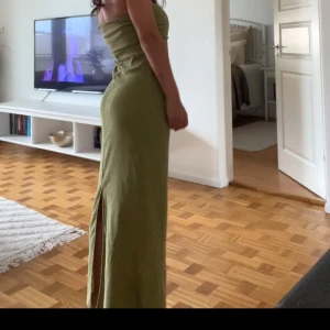 Olivgrön midi bandeauklänning Zara - Säljer en olivgrön bandeauklänning från Zara. Materialet är ribbat och stretchigt, vilket ger en bekväm passform och den har en liten slit back. Klänningen är i storlek 36/s men passar både 38 och även 34/xs vilket jag vanligtvis brukar ha.