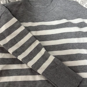 Grå och vit randig tröja - Säljer en stilren grå och vit randig tröja med långa ärmar och ribbade muddar. Perfekt för en avslappnad look. Tröjan har en rund halsringning och är tillverkad i ett mjukt material. Den har även små öppningar vid sidan så den ser snyggare ut. 