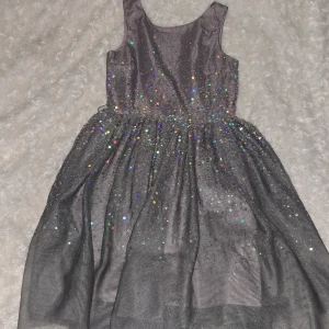 Glittrig klänning från H&M - Säljer en superfin glittrig klänning från H&M i mörkgrått. Klänningen är ärmlös och täckt med glittriga paljetter som ger en festlig look. Perfekt för speciella tillfällen! ✨