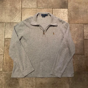 Ralph Lauren Quarter zip Large - Säljer en stilren grå Quarter/Half zip tröja från Polo Ralph Lauren. Tröjan har en dragkedja vid halsen och ett broderat märke på bröstet. Perfekt för en avslappnad och snygg look. Tröjan är i riktigt gott skick!