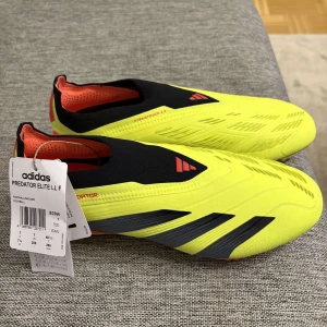 Adidas Predator Elite LL F - Säljer ett par Adidas Predator Elite LL F fotbollsskor i en iögonfallande gul färg med svarta detaljer. Skorna har en strömlinjeformad design utan snörning och en röd sula med dobbar för optimalt grepp på planen. Perfekta för den seriösa fotbollsspelaren. Storlek 40 2/3