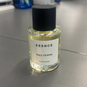 Essnce Très Femme Eau de Parfum - Säljer en elegant flaska av Essnce Très Femme Eau de Parfum. Flaskan är genomskinlig med en stilren svart kork och en enkel etikett. Doften är sofistikerad och feminin, perfekt för den som vill ha något unikt och fräscht.