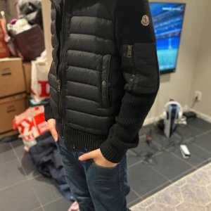 Svart quiltad jacka från Moncler - Snygg svart quiltad jacka från Moncler med dragkedja och huva. Jackan har långa ärmar och en praktisk ficka med dragkedja på ärmen. Perfekt för kyligare dagar.