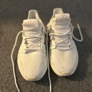 Vita sneakers från Adidas - Snygga vita sneakers från Adidas med en modern design och stickat material. Skorna har snörning och en unik sula som ger extra stilpoäng. Perfekta för en trendig look.