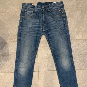 Replay anbass jeans  - Snygga blå jeans från Replay med klassisk femficksdesign och en lätt tvättad look. De har en knappgylf och bälteshällor, vilket gör dem perfekta för en avslappnad stil. Märkesdetaljer syns på bakfickan och linningen.
