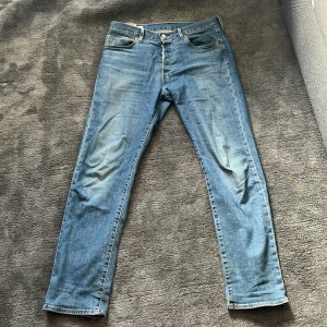 Levis 501 jeans i blå denim - Säljer ett par klassiska Levis 501 jeans i blå denim. De har en straight passform och knappar i gylfen. Perfekta för en avslappnad stil. Märkeslappen sitter på baksidan av midjan.