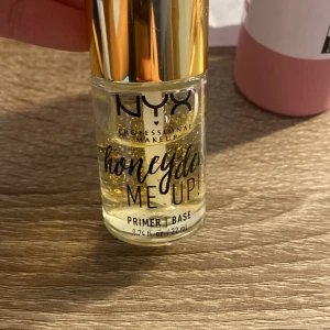 NYX Honey Dew Me Up Primer - NYX Honey Dew Me Up Primer är en lyxig primer med gyllene partiklar som ger en strålande bas för smink. Den kommer i en genomskinlig flaska med guldfärgat lock och innehåller 22 ml. Perfekt för att skapa en jämn och lysande hudton.