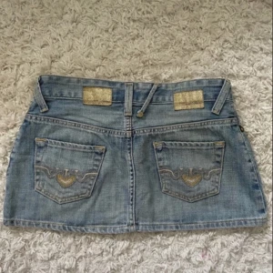 lågmidjad jeans kjol  - Super söt jeans kjol från cross med broderier på bakfickorna 💗.                                                                  Midja: 36cm (mätt platt) Längd: 27cm (mätt platt) 