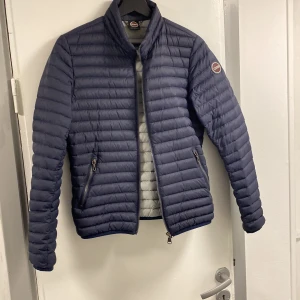 Mörkblå pufferjacka från Colmar - Säljer en snygg mörkblå pufferjacka från Colmar i mycket bra skick. Använd 1-2 gånger. Perfekt för höst och vår, med en stilren design och bekväm passform. Märkeslogga på ärmen ger en extra touch av stil. Passar både till vardags och lite finare tillfällen.