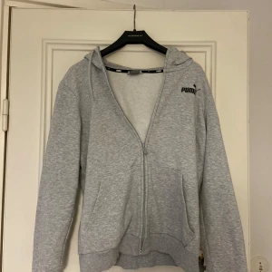 Grå zip-hoodie från Puma - Säljer en grå hoodie från Puma med dragkedja och huva. Tröjan har långa ärmar och en klassisk passform. Perfekt för en avslappnad stil eller träning. 🐾