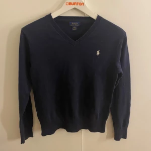 Mörkblå tröja från Polo Ralph Lauren - Säljer en stilren mörkblå tröja från Polo Ralph Lauren med v-ringning och det klassiska logotypbroderiet på bröstet. Tröjan har långa ärmar och är perfekt för en elegant vardagslook. Passar för folk kring 155-160