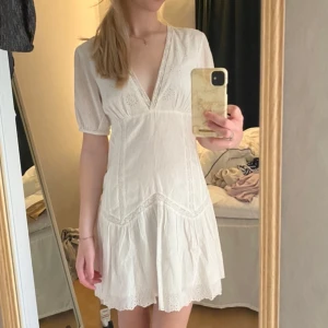 Vit kortklänning med spetsdetaljer - Säljer en söt vit kortklänning med v-ringning och spetsdetaljer. Klänningen har korta ärmar och en luftig passform, perfekt för varma dagar. Den har en romantisk känsla med fina detaljer. Använd 4 gånger.