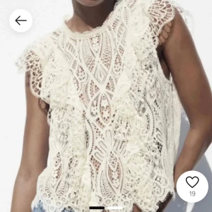 Vit spetsblus - Säljer en vacker vit spetsblus med volangdetaljer. Blusen är ärmlös och har ett intrikat mönster som ger en romantisk känsla. Perfekt för varma dagar eller som ett lager över ett linne.