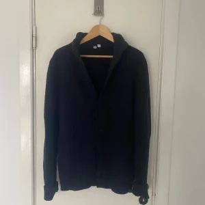 Mörkblå stickad kofta från Uniqlo - Säljer en stilren mörkblå stickad kofta från Uniqlo. Koftan har en ribbad struktur och knappar framtill. Perfekt för kyliga dagar och enkel att matcha med olika outfits. Passar M utmärkt! Skriv om ni har några övriga frågor🙌