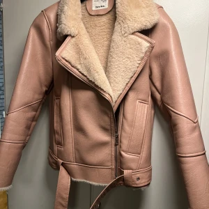 Beige teddyjacka från Zara Kids - Säljer en snygg beige teddyjacka från Zara Kids med mjukt fuskpälsfoder och bred krage. Jackan har skinnimitation på utsidan, dragkedja fram, bälte i midjan och detaljerade sömmar. Långärmad med dragkedja vid ärmslut för extra stilpoäng.