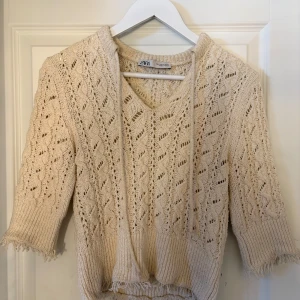 Beige stickad tröja från Zara - Säljer en beige stickad tröja från Zara med snyggt hålmönster och ribbade muddar. Tröjan har v-ringning, snörning vid halsen och trekvartsärmar med fransade kanter. Pris går att diskutera vid snabb och enkel affär
