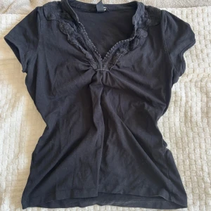 Y2k tröja  - Svart blus i bomull med korta ärmar och djup v-ringning. Kragen och ringningen är dekorerade med fina spetsdetaljer som ger en romantisk vibe. Ger lite Elena Gilbert vibe, och sitter jättefint. 