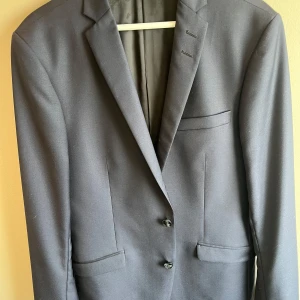 Tiger of Sweden Kavaj  - Snygg svart kavaj från Tiger of Sweden med slät finish. Klassisk passform med två knappar framtill, smala slag och flera fickor. Fodret är elegant. Perfekt för dig som vill ha en stilren look.