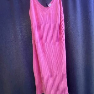 Rosa ribbad ärmlös klänning - Säljer en snygg rosa klänning med ribbad struktur och v-ringad hals. Klänningen är ärmlös och har en kort längd, perfekt för varma dagar. Den har en enkel och stilren design som gör den lätt att matcha med accessoarer.