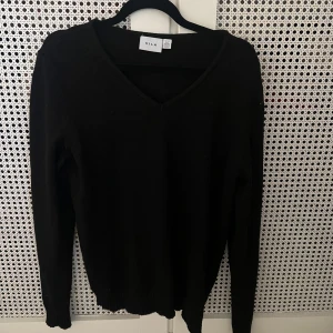 Svart v-ringad tröja från VILA - Svart stickad tröja från VILA med v-ringad hals och långa ärmar. Enkel och stilren design som funkar till många olika outfits. Mjuk och skön kvalitet, perfekt för kyliga dagar. Ribbad kant vid ärmslut och nederkant.