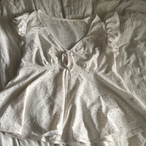 Vit blus med spets och volang - Supersöt vit blus med broderade hålmönster, v-ringning och knyt där fram. Använd ett få tal gånger 💕