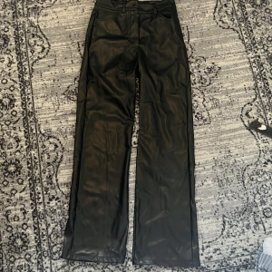 Svarta raka skinnbyxor XS - Snygga svarta byxor från Madlady i skinnimitation. De har raka ben, hög midja och klassisk femficksdesign. Byxorna stängs med dragkedja och knapp framtill. 