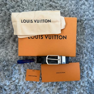 Louis Vuitton svart rutigt skärp - Säljer ett stilrent Louis Vuitton bälte i svart skinn med klassiskt rutigt Damier-mönster. Bältet har en silverfärgad metallspänne och kommer med originalförpackning och dustbag. Perfekt accessoar för dig som gillar lyxiga detaljer och ikonisk design.