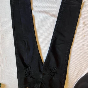 Svarta skinny jeans från Diesel, stl 32 - Svarta jeans från Diesel i storlek 32 med skinny passform. Snygga slitningar vid knäna ger en cool och edgy vibe. Klassisk femficksmodell med Diesel-logga på bakfickan. Jeansen är gjorda i stretchigt bomullsmaterial för skön komfort.