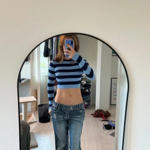 Blå croppad randig tröja från Zara - Säljer en croppad långärmad tröja från Zara med breda marinblå och ljusblå ränder. Tröjan är ribbad och har en slim passform som sitter snyggt på kroppen. Perfekt för dig som gillar en trendig och chill stil.