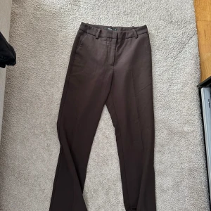 Bruna och svarta kostymbyxor från bikbok - Säljer två par stilrena kostymbyxor från bikbok, ett par i mörkbrunt och ett par i svart. Båda har raka ben, bälteshällor och klassisk midja. Perfekta för dig som vill ha en clean och snygg look. Materialet är mjukt och känns bekvämt mot huden.