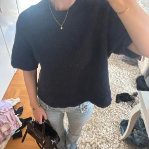 Mörkblå stickad tröja med kort ärm - Säljer en mörkblå stickad tröja med korta ärmar och rund hals. Modellen är loose och har en enkel, clean look som funkar till jeans eller kjol. Materialet är mjukt och lite fluffigt, perfekt för dig som gillar chill vibes och vill ha något bekvämt men snyggt.