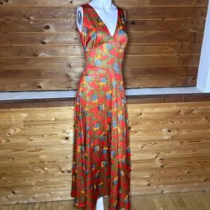 Röd blommig långklänning - Snygg röd långklänning med blommigt mönster i blått och grönt. Klänningen har en v-ringad hals och är ärmlös, vilket ger en elegant look. Perfekt för somriga tillfällen.