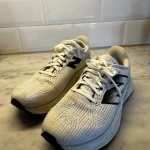 New Balance FuelCell vita sneakers - Säljer ett par vita New Balance FuelCell sneakers med svart logga på sidan. Skorna är i syntetmaterial med stickad ovandel. Perfekta för dig som gillar sportig stil och vill ha bekväma skor till träning eller vardag.