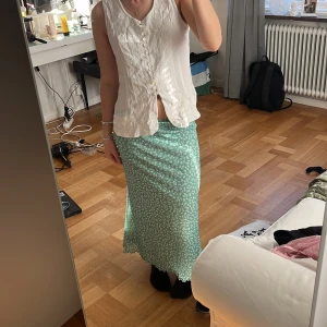 Grön blommig långkjol - Säljer en superfin grön långkjol med vitt blommigt mönster. Kjolen har en mjuk, flowy passform och sitter snyggt i midjan. Perfekt för dig som gillar en chill och feminin stil. Materialet känns lätt och svalt, perfekt för varmare dagar.