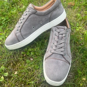 Grå  Christian Louboutins  - Snygga grå sneakers från Christian Louboutin i mjuk mocka med vit platt sula och ikonisk röd undersida. Skorna har rund tå, snörning och diskreta metalldetaljer på sidan. Insidan är beige och ger en clean vibe. Dem är helt äkta. Kontakta mig vid några frågor!